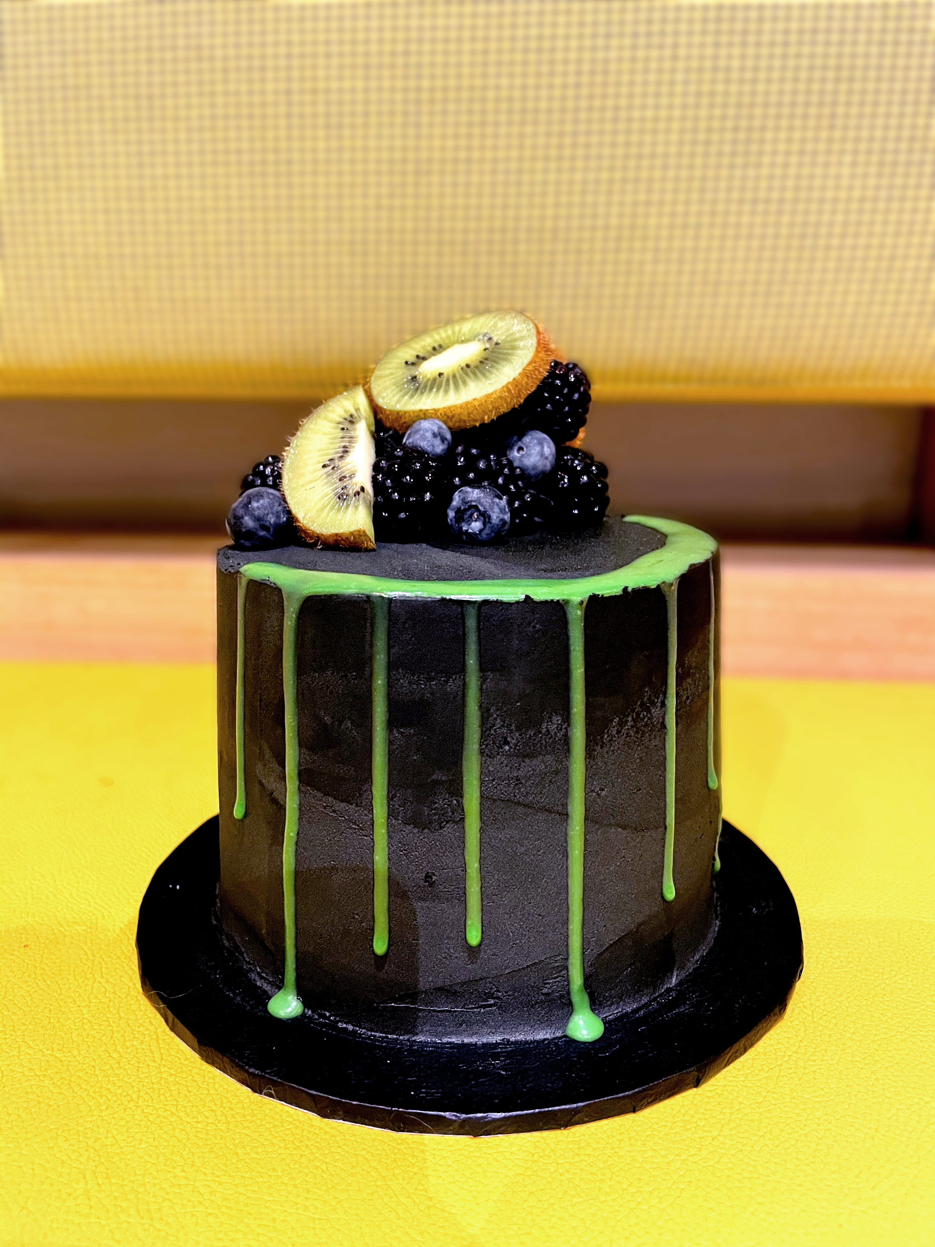 black buttercream cake with green drip decorated with blackberries and kiwis