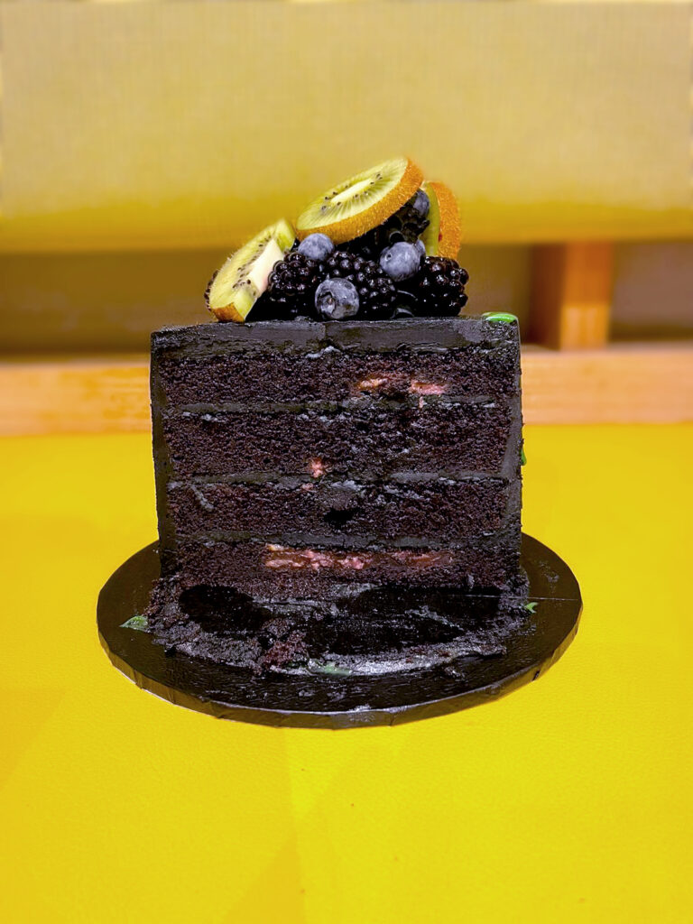 cut open black buttercream cake with green drip decorated with layers studded with berries